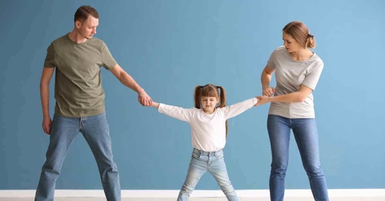 A mom and dad playing a game of "tug of war" with their daughter in the middle
