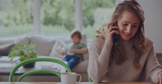 woman speaking on phone with young child in the background sitting on a couch