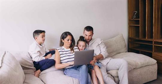 A family sitting on a couch working on a laptop