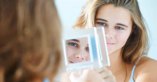 A woman staring at her reflection in a small mirror