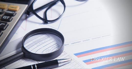 magnifying glass, reading glasses, and a calculator laying on top of a pile of financial reports.