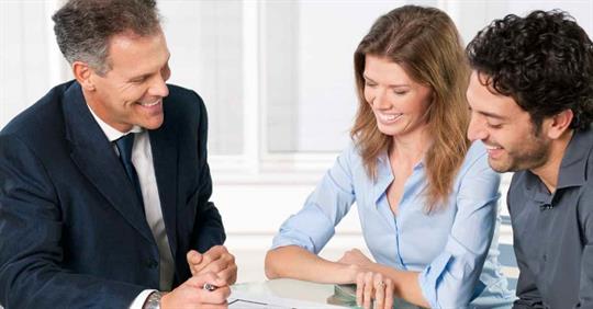 A man and woman smiling as they work with another man. They are looking over a document together.