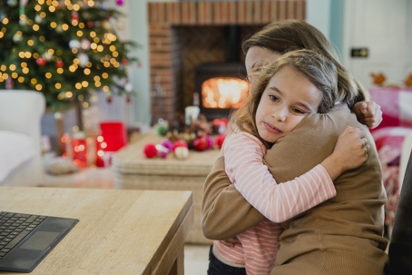 mother and daughter hugging in front of Christmas tree