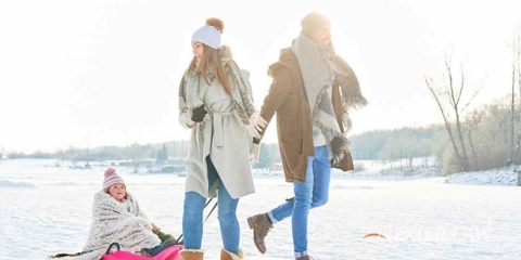 A man and woman dragging their daughter behind them in a sled. Snow covers the ground, and all three people are dressed warmly.